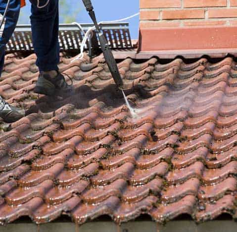 man in oklahoma using a pressure washer to clean a tile roof